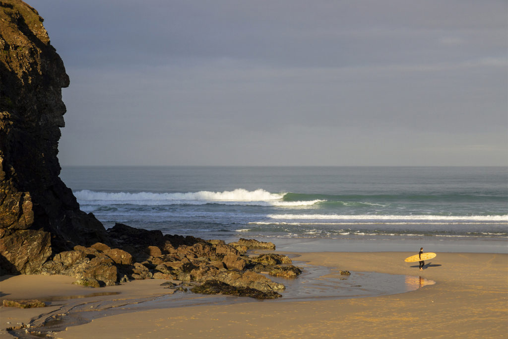 James Otter with his Pieces of Eight wooden surfboard exiting the surf at Chapel Porth, Cornwall.