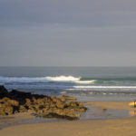 James Otter with his Pieces of Eight wooden surfboard exiting the surf at Chapel Porth, Cornwall.
