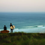 Chris and James Otter look down on the Surf at Perranporth with their wooden surfboards. Fetch and Coaster.