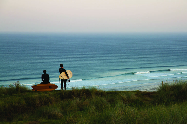 Chris and James Otter look down on the Surf at Perranporth with their wooden surfboards. Fetch and Coaster.
