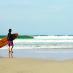 James Otter with the Pier wooden surfboard at Chape Porth, Cornwall in summer.