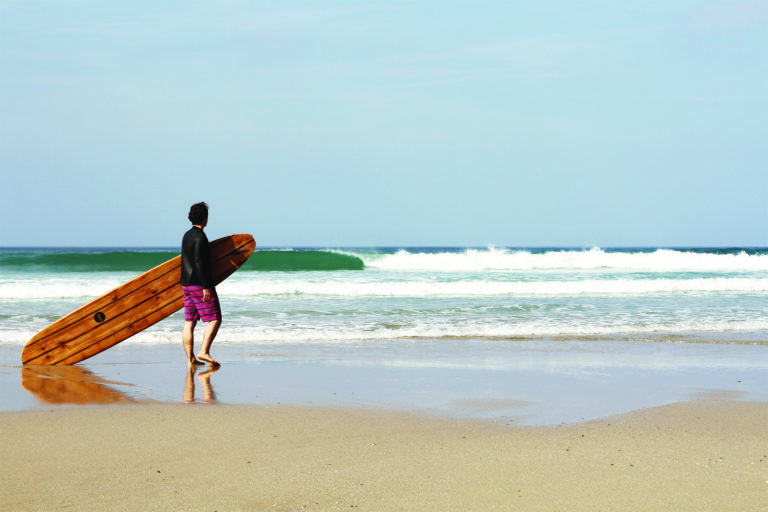 James Otter with the Pier wooden surfboard at Chape Porth, Cornwall in summer.