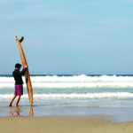James Otter with the Pier wooden surfboard at Chape Porth, Cornwall in summer.