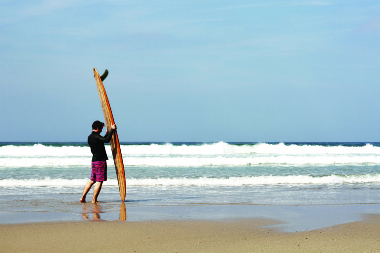 James Otter with the Pier wooden surfboard at Chape Porth, Cornwall in summer.