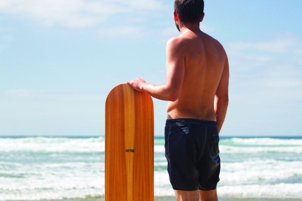 Chris stands with the otter surfboards wooden bellyboard in his Riz Boardshorts
