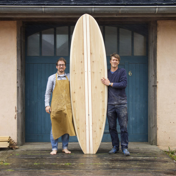 Dory - David and James Otter outside the blue workshop doors with an Otter surfboards wooden paddle board