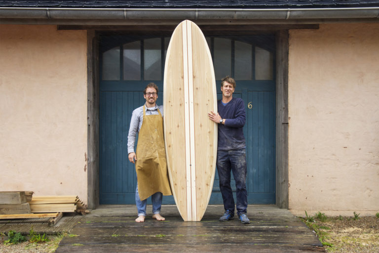 Dory - David and James Otter outside the blue workshop doors with an Otter surfboards wooden paddle board