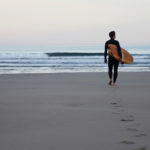 James Otter walking out to the surf at Chapel Porth, Cornwall with his fetch wooden surfboard.