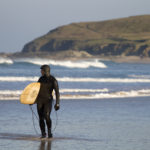 James Otter looks back on a few waves with his wooden surfboard Coaster under his Arm in his Finisterre wetsuit.