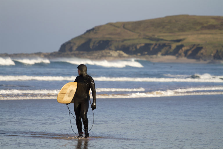 James Otter looks back on a few waves with his wooden surfboard Coaster under his Arm in his Finisterre wetsuit.