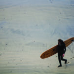 Mat Arney walks back across the sand at Gwithian with his wooden Otter Surfboards Pier.