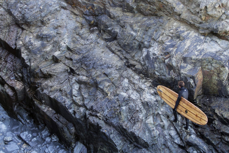 Chris walks back up the cliff with the Otter Surfboards wooden longboard Seasaw at Godrevy