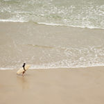 Marcus exits the surf with the Otter Surfboards Wooden Coaster at Chapel Porth, Cornwall. sandy beach