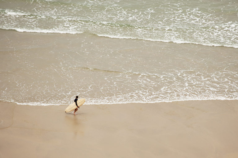 Marcus exits the surf with the Otter Surfboards Wooden Coaster at Chapel Porth, Cornwall. sandy beach