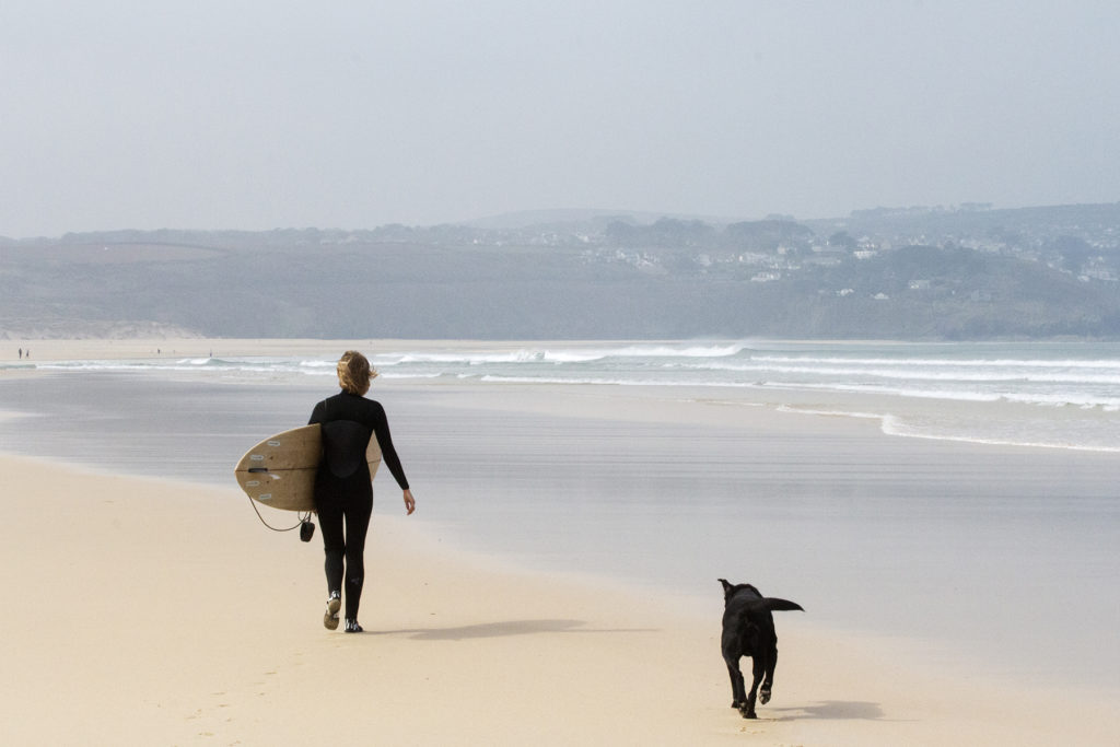 Sophie Hellyer walks along a sandy beach in the wind at st Ives bay with buddy the dog and her otter surfboards wooden surfboard Coaster