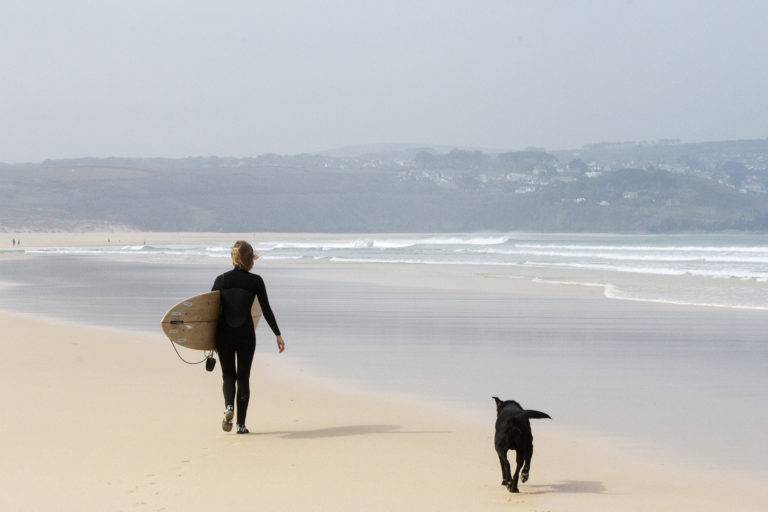 Sophie Hellyer walks along a sandy beach in the wind at st Ives bay with buddy the dog and her otter surfboards wooden surfboard Coaster