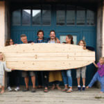 Family with wooden paddleboard outside the otter surfboards workshop with Chris and James