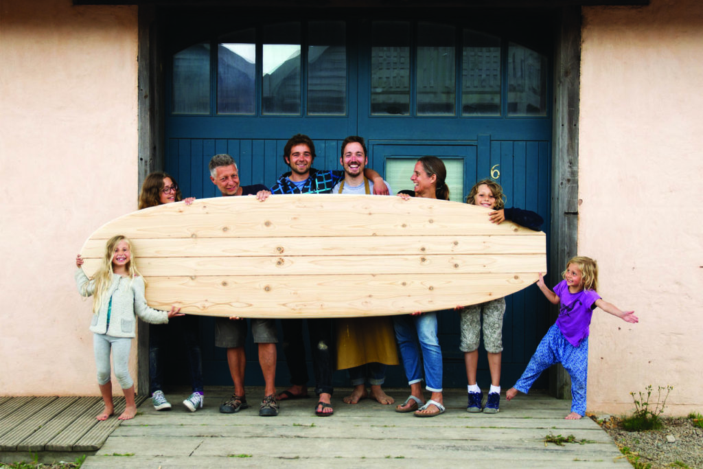 Family with wooden paddleboard outside the otter surfboards workshop with Chris and James