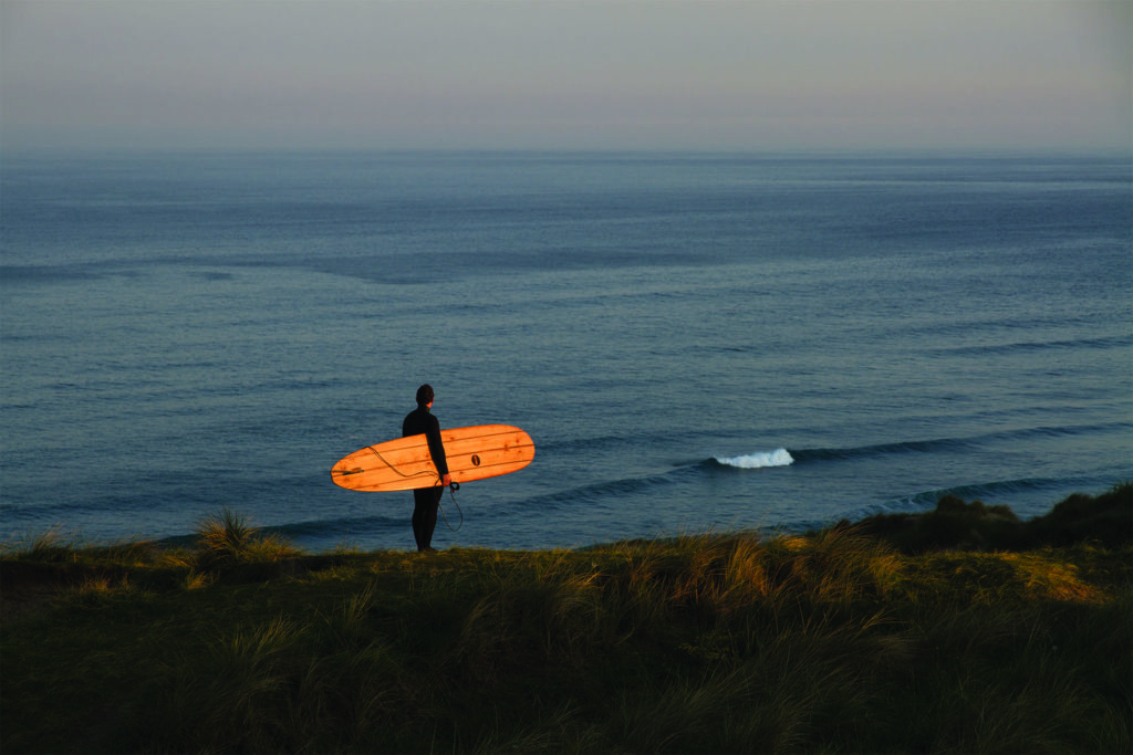 James Otter Seasaw at Perran Sands Wooden Surfboard with surfer on the coast in Cornwall