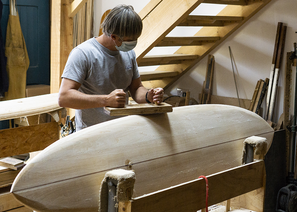 Hugh sanding the rail of his wooden surfboard in the otter workshop