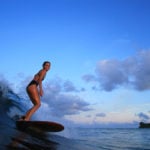 Sophie Hellyer on the beach in wetsuit with otter wooden surfboard in maldives seadar