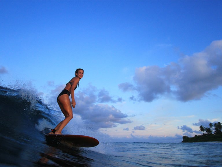Sophie Hellyer on the beach in wetsuit with otter wooden surfboard in maldives seadar