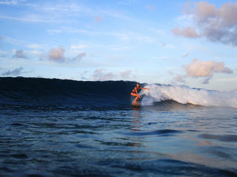 Sophie Hellyer on the beach in wetsuit with otter wooden surfboard in maldives seadar