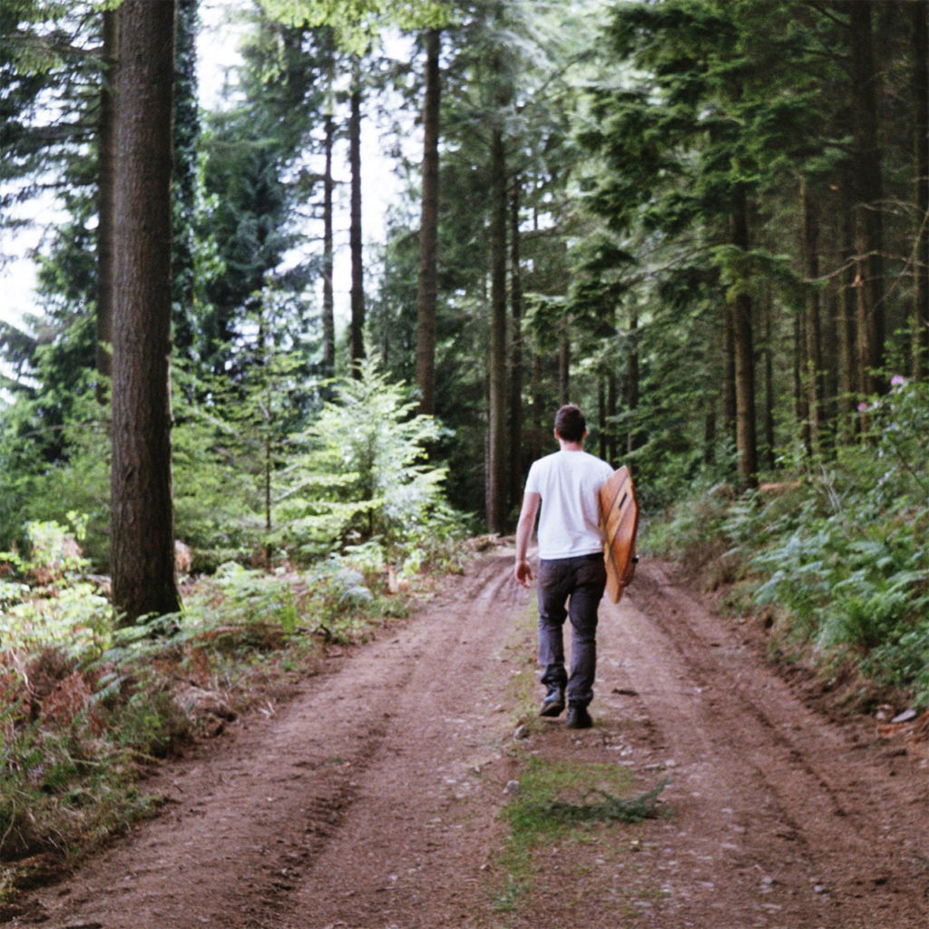 The Storyboard by James Otter and Mat Arney Wooden Surfboard Project James walking through woods with wooden surfboard