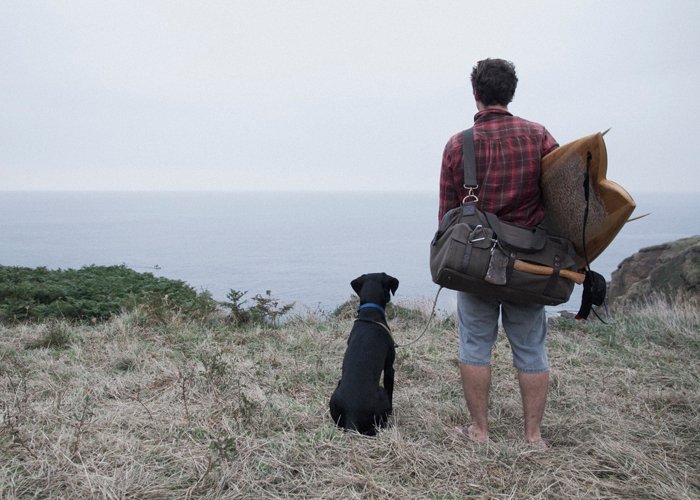 James Otter and Buddy with wooden surfboard on cliff top