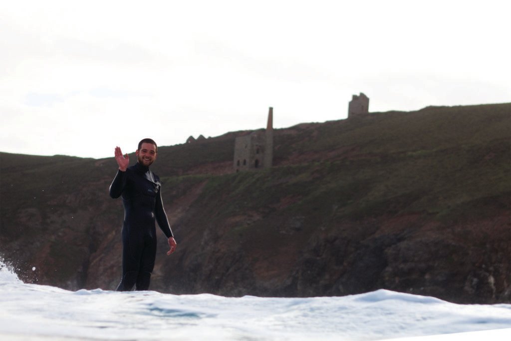 Chris waving as he surfs past chapel porth