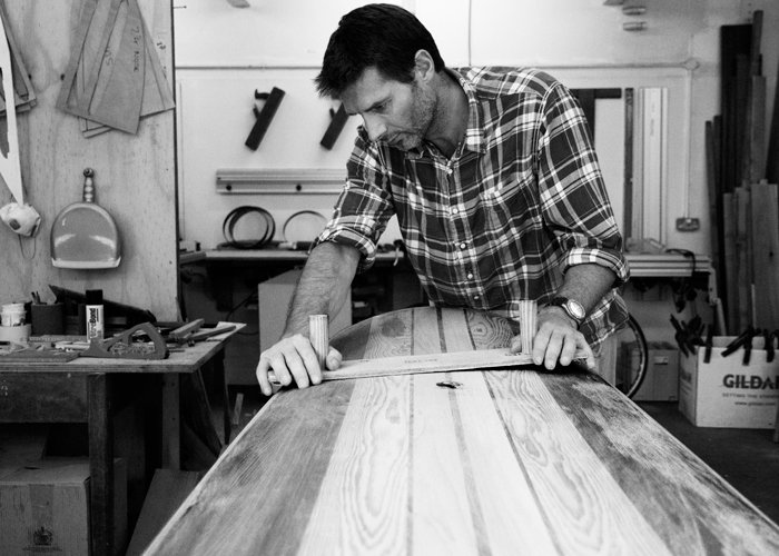 Tim sanding fairing his wooden longboard surfboard in the otter workshop
